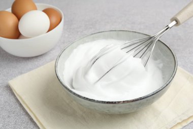 Beyazları kasede çırpmak, çırpmak ve yumurtaları gri desenli masada çırpmak, yakın plan