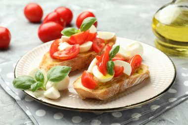Mozarella peynirli, domatesli ve fesleğenli lezzetli bruschettalar. Gri desenli masa, yakın plan.