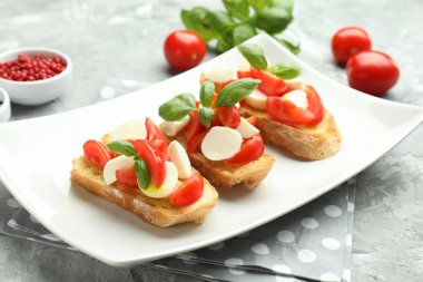 Mozarella peynirli, domatesli, fesleğenli ve baharatlı lezzetli bruschettalar. Gri desenli masa, yakın plan.