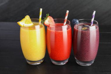 Siyah ahşap masadaki malzemelerle bardaktaki farklı lezzetli içecekler.