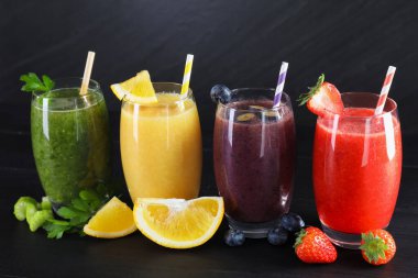 Farklı tatlarda bardaklar ve siyah ahşap masada malzemeler.