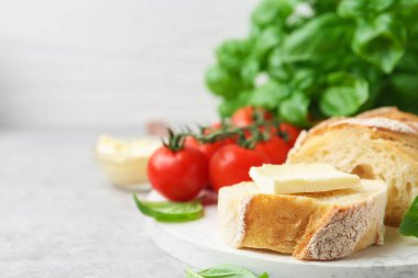 Açık gri masada tereyağlı, fesleğenli ve domatesli baget dilimleri, yakın plan. Metin için boşluk