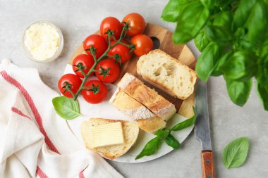 Tereyağlı baget dilimleri, fesleğen, domates ve bıçak açık gri masada, düz yatıyordu.