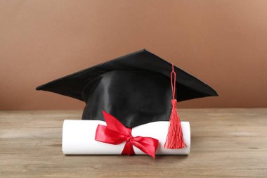Mezuniyet şapkası ve diploması ahşap masada, kahverengi arka planda, yakın plan.