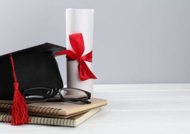 Mezuniyet şapkası, diploma, defterler ve gözlük beyaz ahşap masa ve arka planda. Metin için boşluk