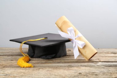 Mezuniyet şapkası ve diploması açık arkaplanda, ahşap masada.