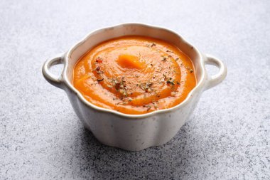 Balkabağı kremalı çorba, kabak şeklindeki kasede servis edilir. Gri masada, yakın plan.