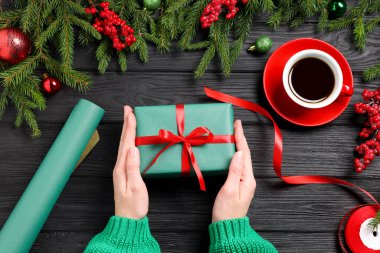 Hediye kutusu olan bir kadın, aromatik kahve ve siyah ahşap masada Noel dekoru.