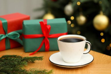 Fincanda romatik kahve, köknar ağacı dalları ve ahşap masada bulanık ışıklara karşı hediye kutuları, yakın çekim. Noel tebrik kartı.