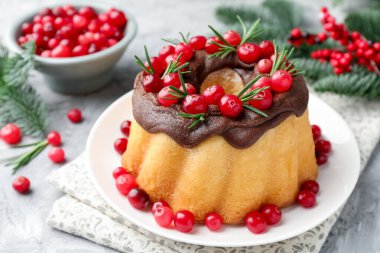 Çikolata kaplı lezzetli Noel pastası, açık gri desenli masada kızılcık ve biberiye, yakın plan.