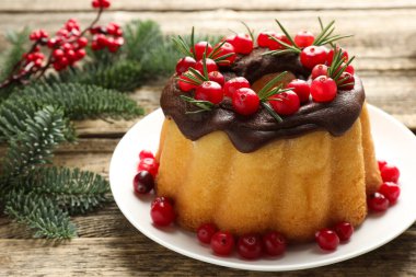 Çikolata kaplı lezzetli Noel pastası, kızılcık, biberiye ve köknar ağacı dalları ahşap masada, yakın plan.