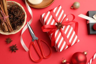 Kutlama ambalajı. Hediye kutuları, kurdele, makas, ambalaj kağıdı ve kırmızı arka planda Noel dekoru, düz yatış