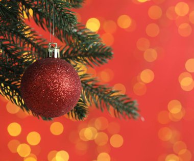 Kırmızı arka planda takıları olan, bulanık ışıkları olan bir Noel ağacı dalı. Mesaj için yer var. Bokeh etkisi