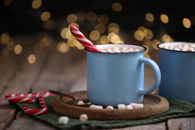 Ahşap masada lokum ve şeker kamışlı lezzetli kakao bulanık Noel ışıklarına karşı, yakın plan. Metin için boşluk