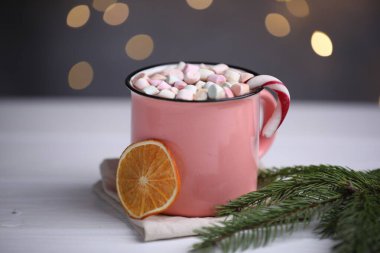 Lezzetli kakao, şekerleme kamışı, kurutulmuş portakal dilimi ve köknar dalı beyaz ahşap masa üzerinde bulanık Noel ışıklarına karşı, yakın çekim