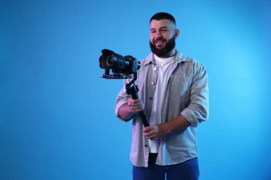 Kameraman açık mavi arkaplanda kameralı titreşimli dengeleyici kullanıyor. Metin için boşluk