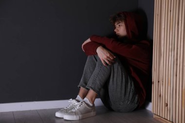 Siyah duvarın yanında depresif bir genç çocuk var.