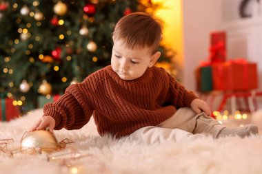 Noel için dekore edilmiş odada yerde oturan sevimli küçük bebek.