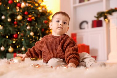 Noel için dekore edilmiş odada yerde oturan sevimli küçük bebek.