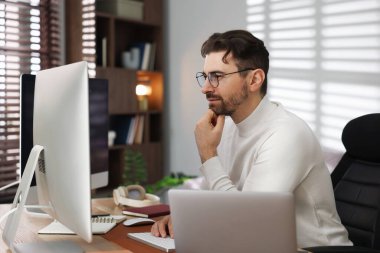 Ofisteki bilgisayarda çalışan gözlüklü programcı