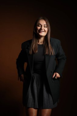 Koyu kahverengi arka planda poz veren şık elbiseli güzel bir genç kadın.