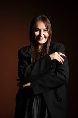 Koyu kahverengi arka planda poz veren şık elbiseli güzel bir genç kadın.