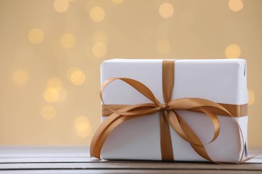 Tahta masanın üzerinde kahverengi kurdeleli güzel bir hediye kutusu bulanık ışıklarla altın bir zemin üzerinde, metin için yeri olan yakın plan. Bokeh etkisi