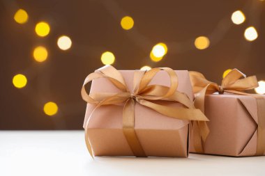 Kahverengi arkaplanlı, beyaz masadaki güzel hediye kutuları. Bulanık ışıklı, yazı için yeri olan. Bokeh etkisi