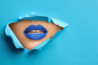 Mavi rujlu genç bayan, yakın plan. Açık mavi kağıttaki yırtık delikten dudaklara bak
