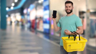 Süpermarkette elinde boş bir alışveriş sepeti ve cep telefonu tutan bir adam. Pankart tasarımı