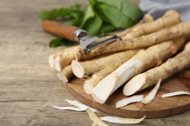 Taze çiğ yaban turpu kökleri, soyucu ve yapraklar ahşap masada, yakın plan. Metin için boşluk