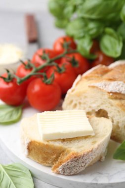 Açık gri masada tereyağlı, fesleğenli ve domatesli baget dilimleri, yakın plan.