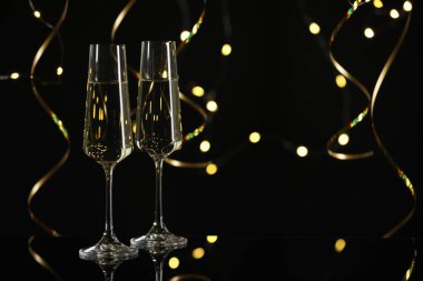 Yeni yıl kutlaması. Flüt bardaklarında köpüklü şarap ve siyah arka planda yılan şeklinde flamalar, bokeh ışıkları.