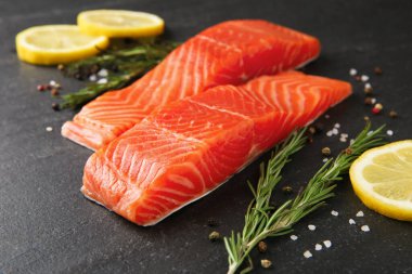 Somon filetosu, baharat ve limon parçaları siyah masada, yakın plan.