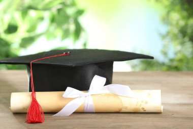 Mezuniyet şapkası ve diploması ahşap masada bulanık arka planda, yakın planda. Metin için boşluk