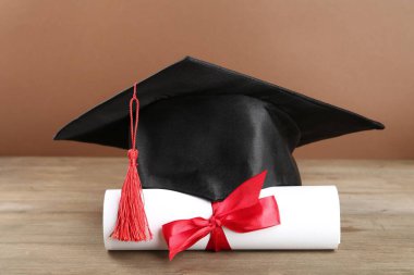 Mezuniyet şapkası ve diploması ahşap masada, kahverengi arka planda, yakın plan.