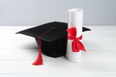 Mezuniyet şapkası ve diploması beyaz ahşap masada, arka planda ışığa karşı, yakın plan.