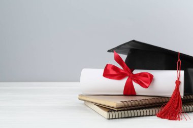 Mezuniyet şapkası, diploma ve arka planda beyaz ahşap masaya dizilmiş defterler. Metin için boşluk