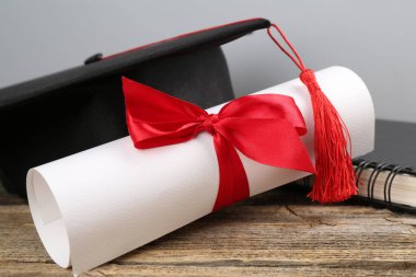 Mezuniyet şapkası, diploma ve defter ahşap masanın üzerinde, arka planda ışığa karşı, yakın plan.