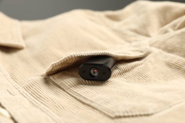 Gri arka planda gömlek cebinde gizli casus kamerası, yakın plan.