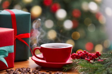 Bardakta romatik kahve, fasulye, köknar ağacı dalları ve ahşap masada bulanık ışıklara karşı hediye kutuları, yakın çekim. Noel tebrik kartı.