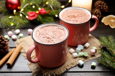 Bardaklarda lezzetli sıcak kakao içecekler, marşmelovlar ve ahşap masada Noel dekoru, yakın plan.