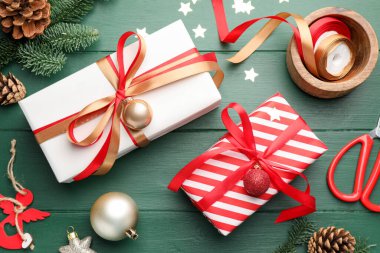 Kutlama ambalajı. Hediye kutuları, kurdeleler, makas, ambalaj kağıdı ve yeşil ahşap masa üzerindeki Noel dekoru, düz yatış