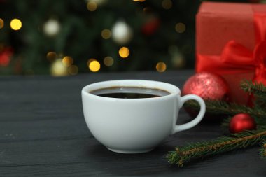 Aromatik kahve ve Noel dekoru ahşap masada bulanık ışıklara karşı, yakın plan.