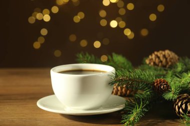 Aromatik kahve ve Noel dekoru ahşap masada bulanık ışıklara karşı, yakın plan.