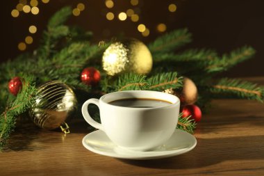 Aromatik kahve ve Noel dekoru ahşap masada bulanık ışıklara karşı, yakın plan.
