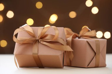 Güzel hediye kutuları beyaz masada kahverengi arka planda bulanık ışıklarla, yakın plan. Bokeh etkisi
