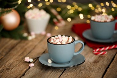 Ahşap masada lokum kaplı lezzetli kakao bulanık Noel ışıklarına karşı, yakın plan.