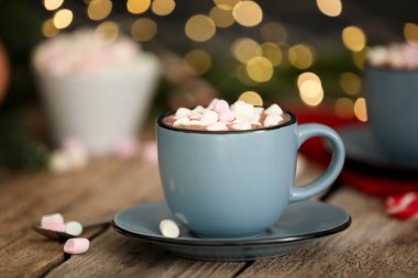 Ahşap masada lokum kaplı lezzetli kakao bulanık Noel ışıklarına karşı, yakın plan.