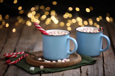 Ahşap masanın üzerinde lokum ve şeker kamışlı lezzetli kakao bulanık Noel ışıklarına karşı, yakın plan.